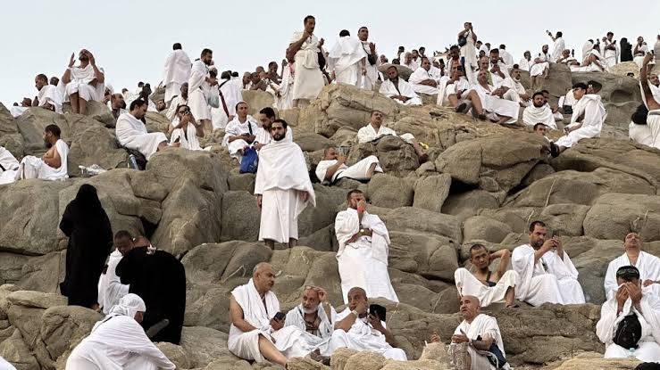 حجاج بالإحرام واقفون على صخور جبل الرحمة في صعيد عرفات يدعون